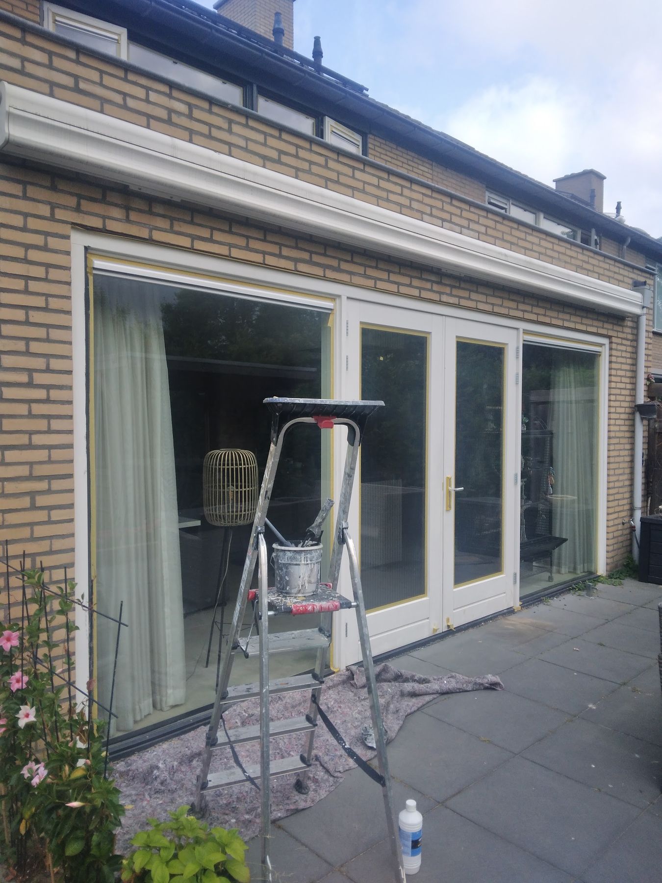 Achtergevel met net geschilderde witte kozijnen en schuifpui, trapje en afdekkleed nog op het terras