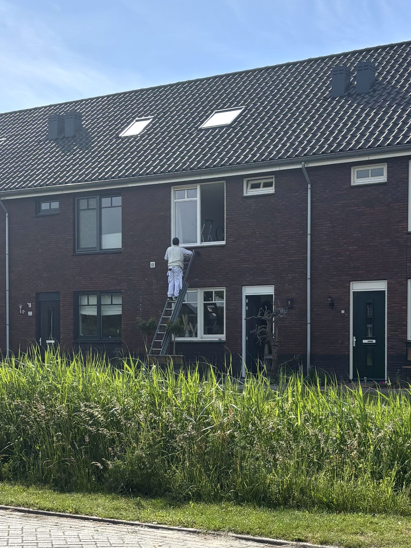 Habib op een ladder aan het schilderen bij een rij nieuwbouwwoningen