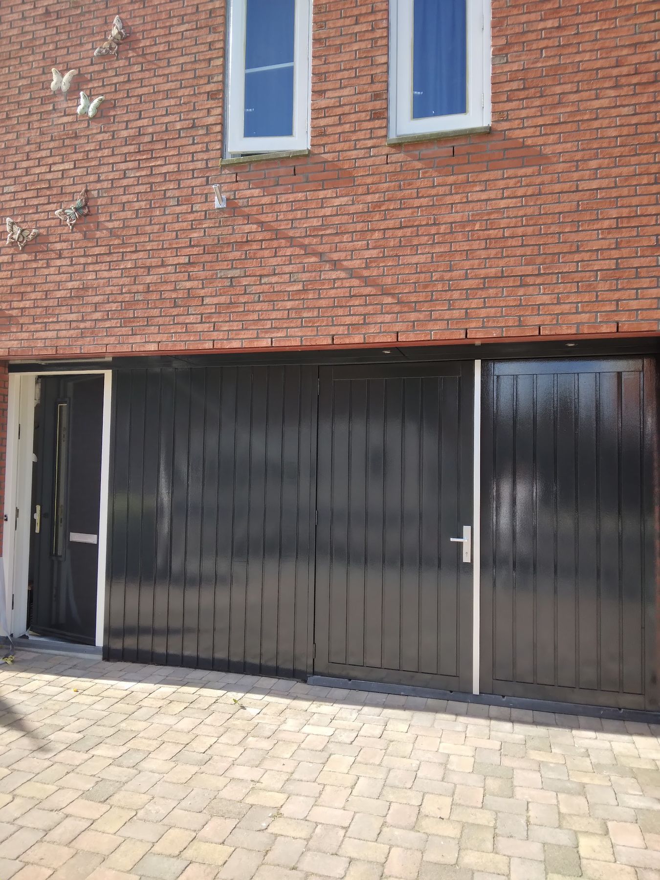Rode bakstenen gevel met zwart gelakte garagedeuren en witte kozijnen