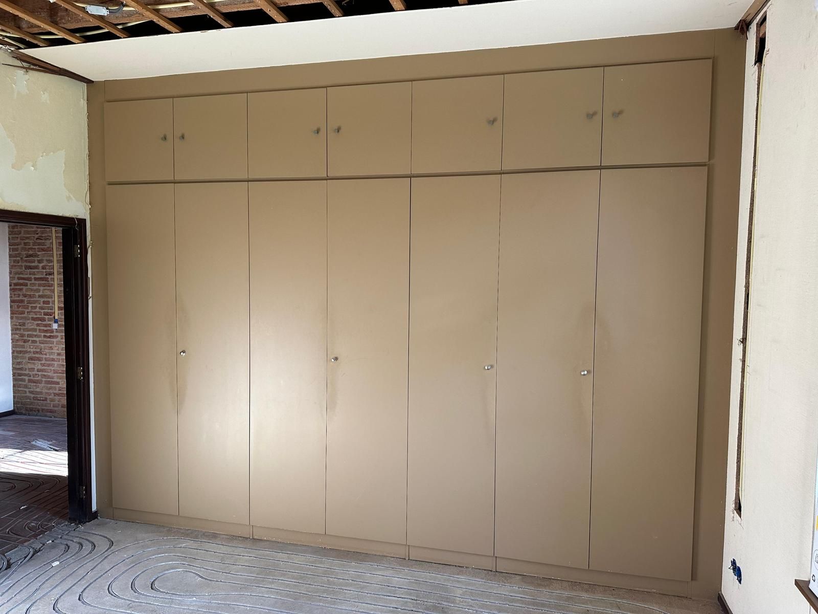 Een volledige wand met inbouwkasten, geschilderd in een warme zandkleur